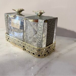 two-piece glass storage jar set with a gold bird lid and decorative tray.